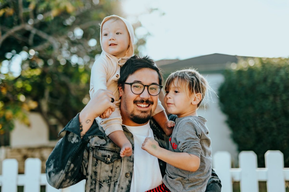 Father holding his two young kids outside their home